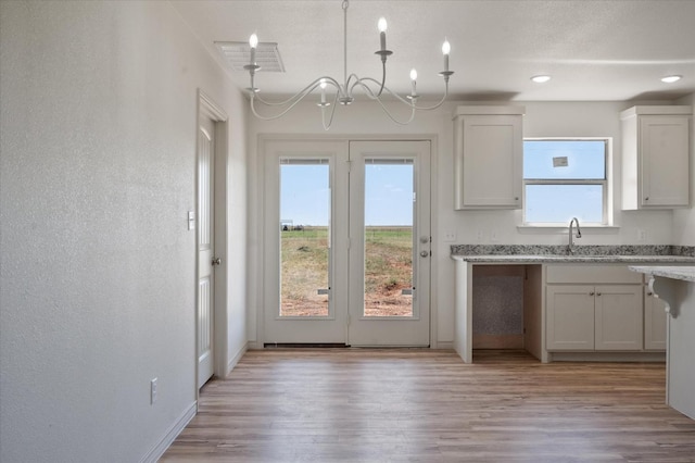 kitchen featuring decorative light fixtures, white cabinetry, sink, light stone countertops, and light wood-type flooring