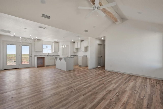 unfurnished living room with sink, hardwood / wood-style flooring, beam ceiling, high vaulted ceiling, and ceiling fan with notable chandelier