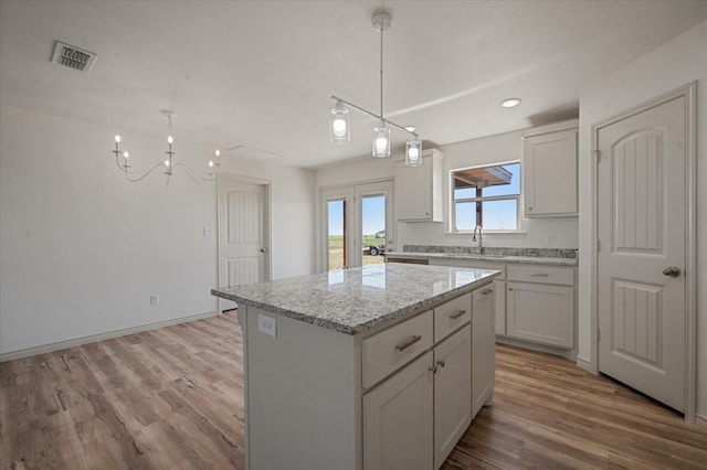 kitchen featuring a kitchen island, decorative light fixtures, white cabinetry, sink, and light stone countertops