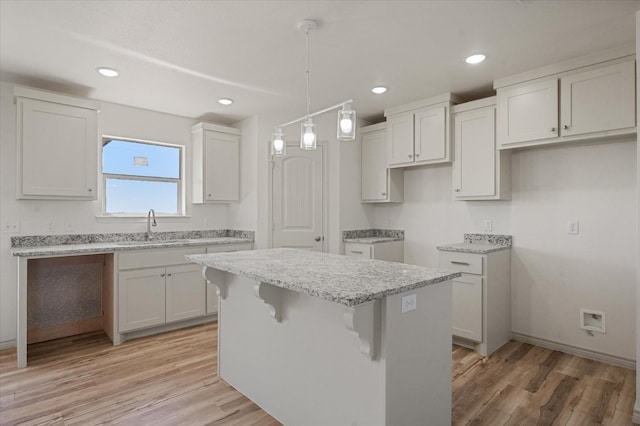 kitchen with sink, light hardwood / wood-style flooring, white cabinetry, hanging light fixtures, and a kitchen island