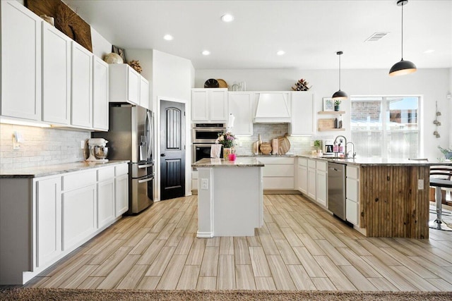 7502 103rd St, Lubbock, TX 79424 - kitchen with stainless steel appliances, decorative backsplash, a center island, custom exhaust hood, and light wood-style flooring