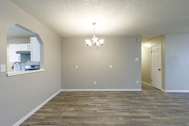 unfurnished dining area featuring dark hardwood / wood-style flooring, a chandelier, and a textured ceiling