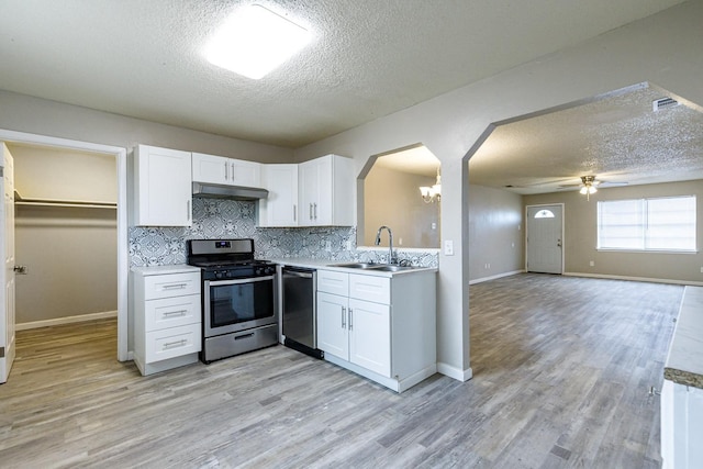 kitchen with sink, appliances with stainless steel finishes, white cabinetry, backsplash, and range hood