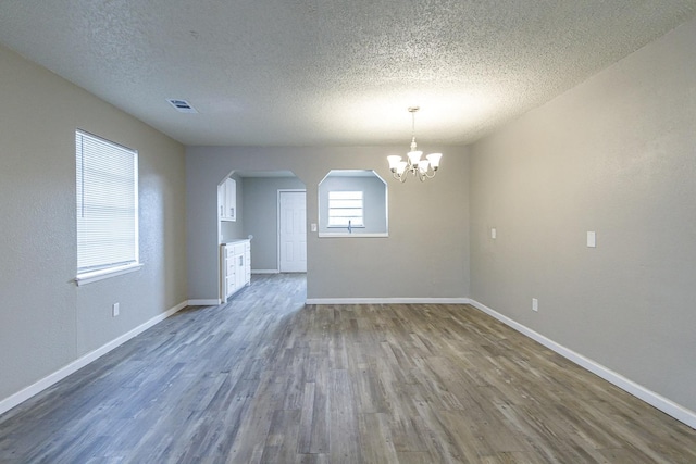 empty room featuring wood-type flooring, a chandelier, and a textured ceiling