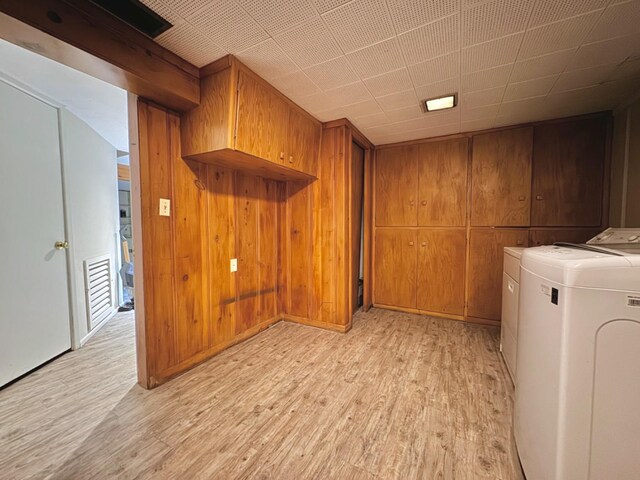 clothes washing area featuring wood walls, washing machine and dryer, cabinets, and light wood-type flooring