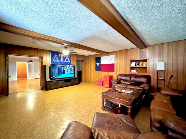 living room featuring ceiling fan, beam ceiling, a textured ceiling, and wood walls