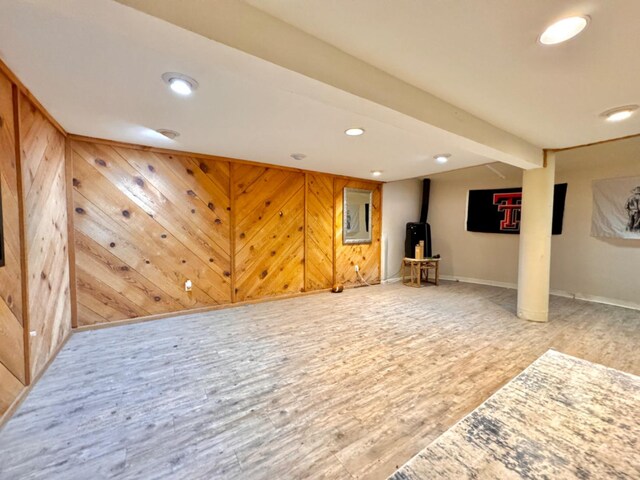 basement featuring hardwood / wood-style floors, wooden walls, and a wood stove