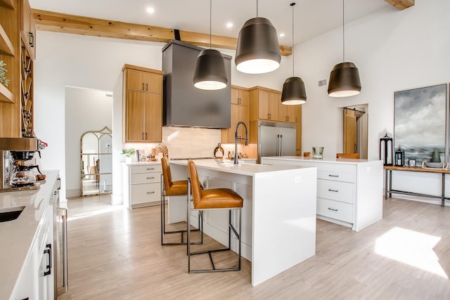 kitchen featuring a breakfast bar, white cabinetry, hanging light fixtures, built in fridge, and a kitchen island with sink