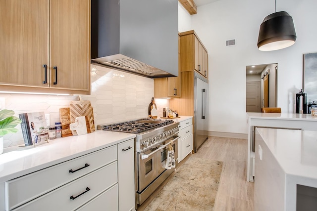 kitchen with wall chimney exhaust hood, hanging light fixtures, premium appliances, decorative backsplash, and white cabinets