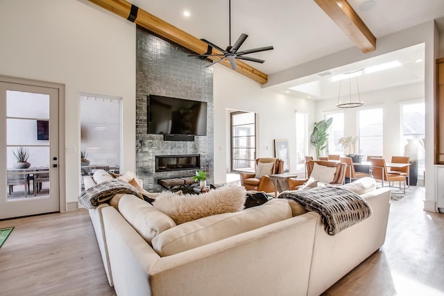 living room with a towering ceiling, a fireplace, light wood-type flooring, ceiling fan, and beam ceiling