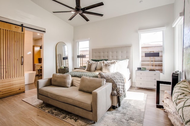 bedroom featuring lofted ceiling, a barn door, connected bathroom, and light hardwood / wood-style flooring