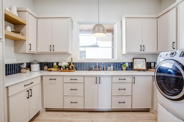 laundry room featuring washer / clothes dryer, sink, cabinets, and light hardwood / wood-style flooring