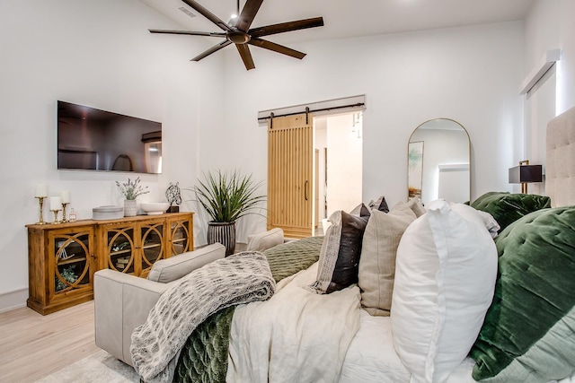 bedroom featuring ceiling fan, lofted ceiling, a barn door, and light hardwood / wood-style flooring