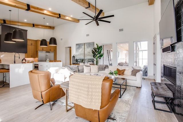 living room with beamed ceiling, a towering ceiling, a fireplace, and light hardwood / wood-style flooring