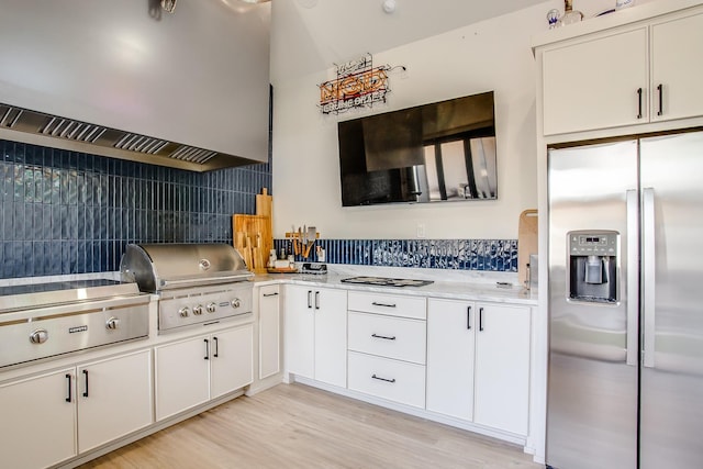 kitchen with extractor fan, white cabinetry, light hardwood / wood-style flooring, stainless steel fridge, and decorative backsplash