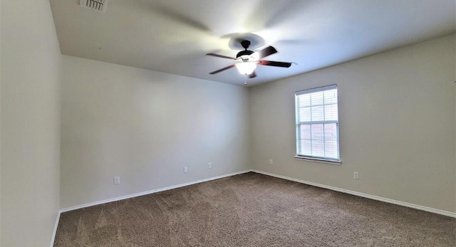 spare room with dark colored carpet, visible vents, ceiling fan, and baseboards