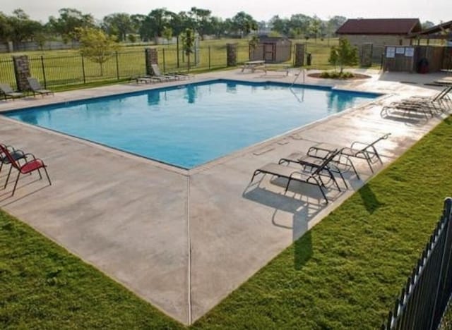 community pool with a patio, fence, and a lawn
