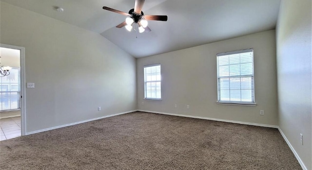 carpeted spare room with ceiling fan with notable chandelier, baseboards, a healthy amount of sunlight, and vaulted ceiling