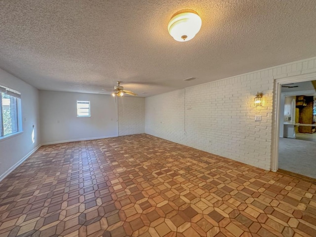 unfurnished room with brick wall, a textured ceiling, and ceiling fan