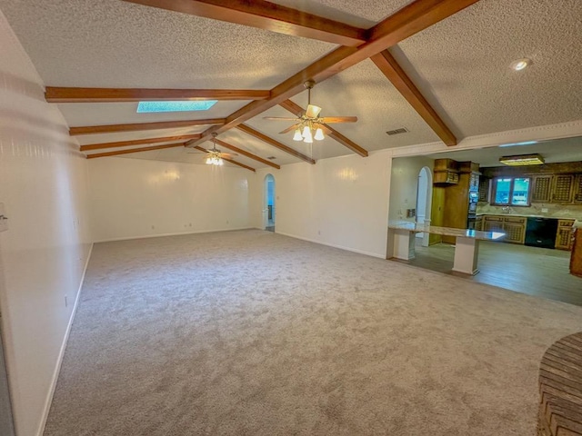 unfurnished living room with ceiling fan, a textured ceiling, carpet floors, and vaulted ceiling with skylight