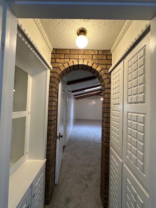 hallway with beam ceiling, dark carpet, a textured ceiling, and brick wall