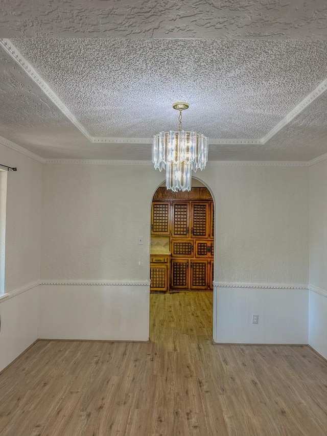 empty room featuring crown molding, hardwood / wood-style floors, a tray ceiling, a textured ceiling, and a chandelier