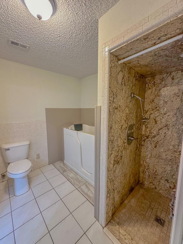 bathroom featuring tile walls, tile patterned flooring, tiled shower, toilet, and a textured ceiling