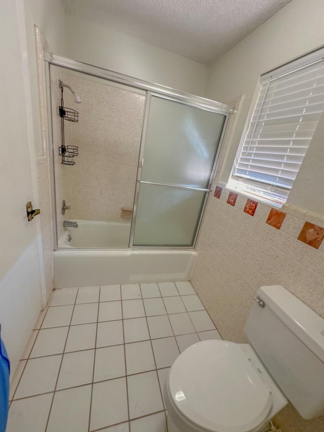 bathroom featuring tile patterned floors, toilet, a textured ceiling, tile walls, and enclosed tub / shower combo