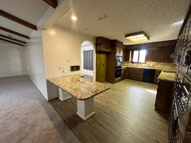 kitchen featuring tasteful backsplash, a textured ceiling, a kitchen breakfast bar, kitchen peninsula, and black appliances