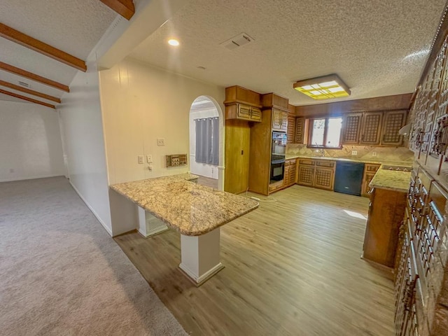 kitchen with a kitchen breakfast bar, black appliances, a textured ceiling, kitchen peninsula, and light wood-type flooring