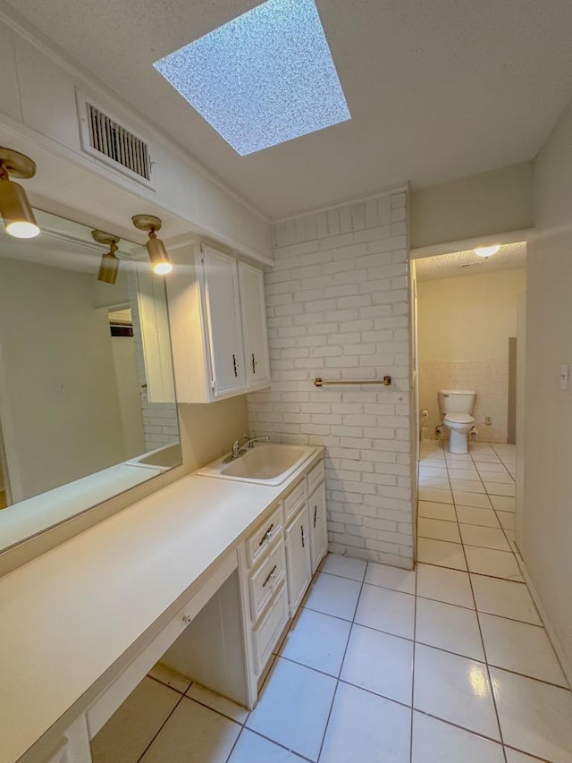 bathroom with tile patterned flooring, toilet, brick wall, and a skylight