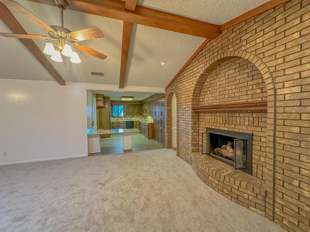 unfurnished living room with carpet floors, vaulted ceiling with beams, ceiling fan, a brick fireplace, and a textured ceiling