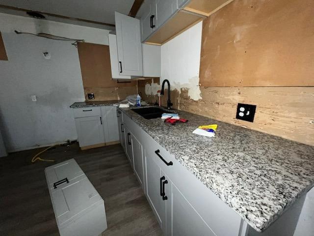 kitchen featuring white cabinetry, sink, dark hardwood / wood-style flooring, light stone counters, and kitchen peninsula