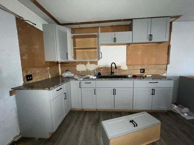 kitchen featuring sink, dark wood-type flooring, white cabinetry, dark stone countertops, and kitchen peninsula