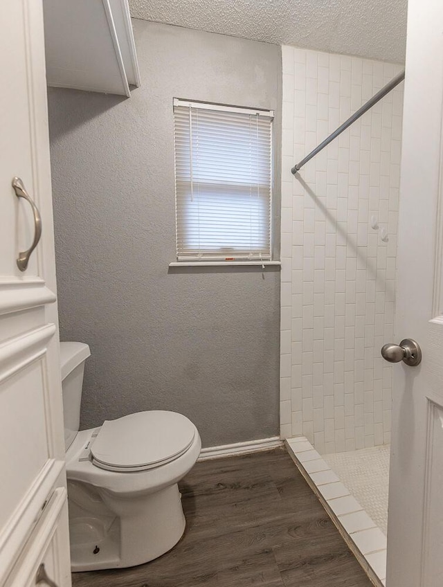 bathroom with hardwood / wood-style flooring, a textured ceiling, toilet, and tiled shower