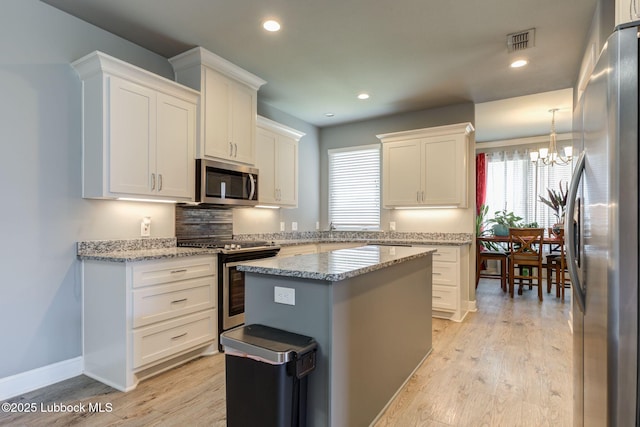 136 Preston Hollow Ln, Wolfforth, TX 79382 - kitchen with appliances with stainless steel finishes, a chandelier, white cabinetry, light wood-style floors, and light stone counters