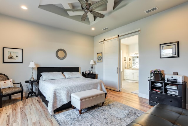 bedroom featuring ceiling fan, ensuite bathroom, a barn door, and light wood-type flooring