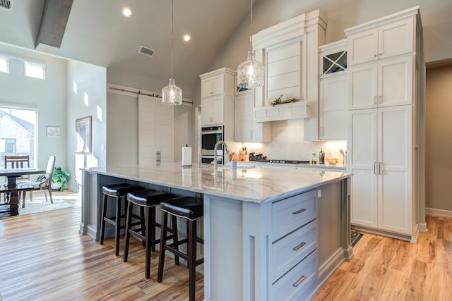 kitchen with a large island, hanging light fixtures, white cabinetry, and a barn door