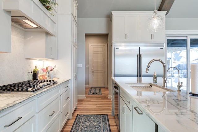 kitchen featuring appliances with stainless steel finishes, decorative light fixtures, sink, white cabinets, and light hardwood / wood-style floors