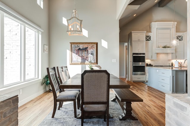 dining room with an inviting chandelier, beam ceiling, high vaulted ceiling, and light wood-type flooring