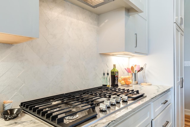 kitchen featuring light stone counters, backsplash, white cabinetry, and stainless steel gas cooktop