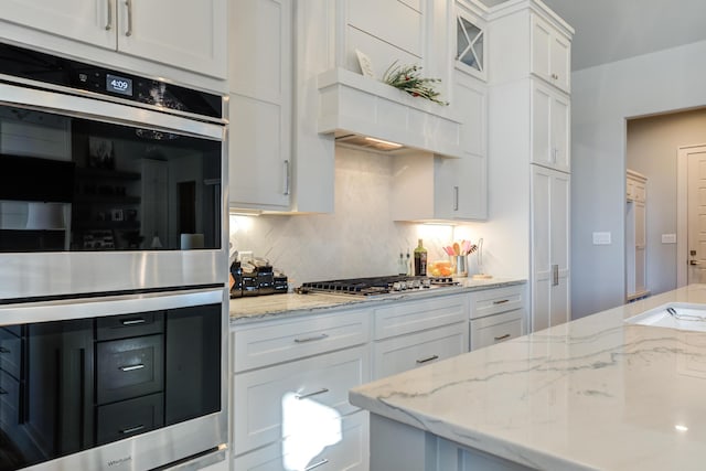 kitchen with stainless steel appliances, light stone countertops, white cabinets, and backsplash