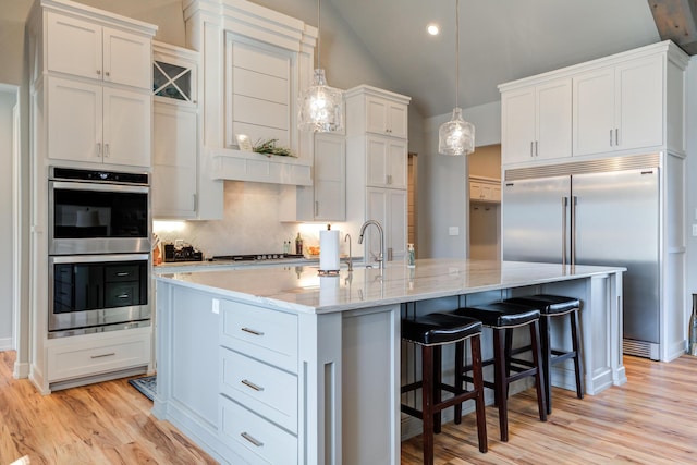 kitchen featuring appliances with stainless steel finishes, white cabinetry, hanging light fixtures, a kitchen breakfast bar, and a center island with sink