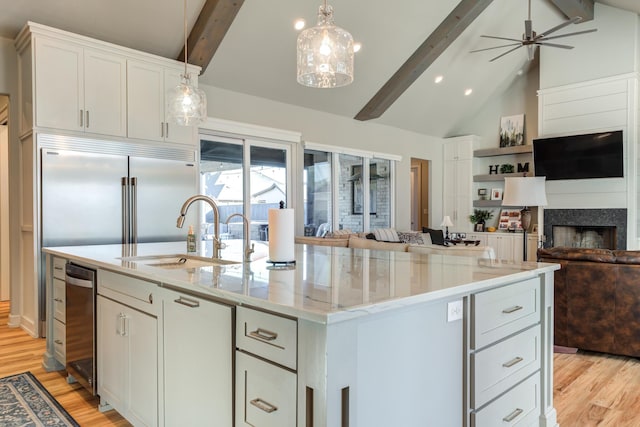 kitchen featuring sink, pendant lighting, beamed ceiling, light stone countertops, and a kitchen island with sink