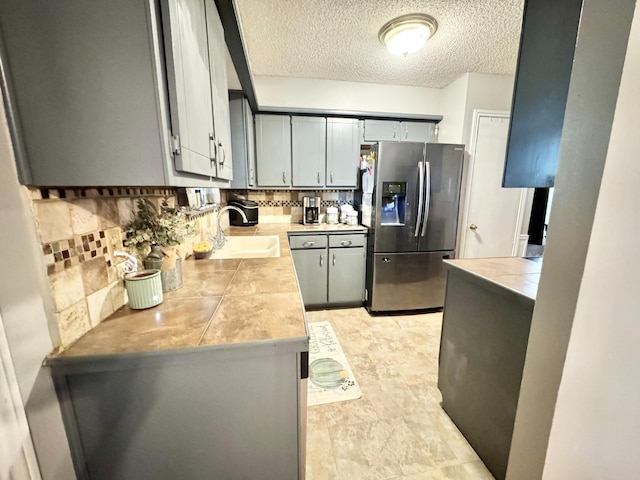 kitchen with gray cabinets, sink, stainless steel fridge, decorative backsplash, and a textured ceiling