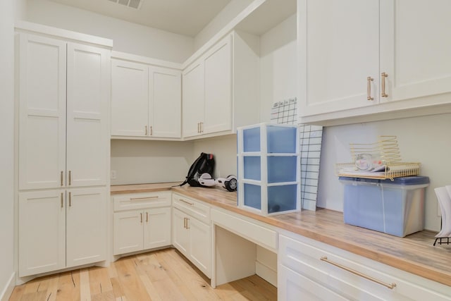 interior space with built in desk, butcher block counters, visible vents, white cabinetry, and light wood-type flooring