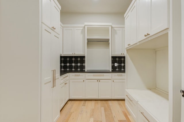 kitchen featuring light wood-style flooring, dark countertops, white cabinetry, and backsplash