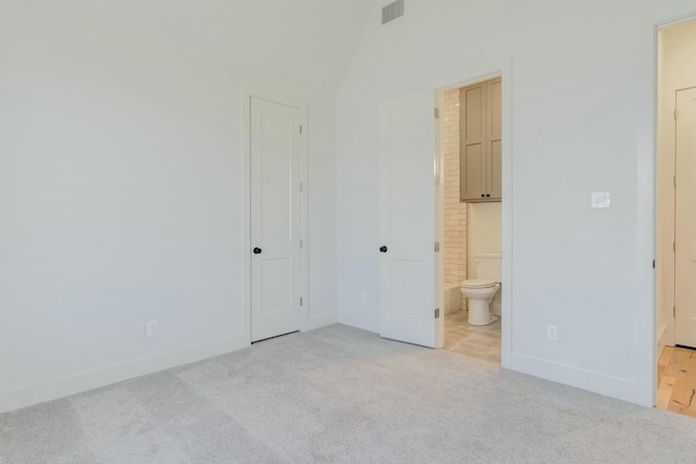 unfurnished bedroom with lofted ceiling, light carpet, visible vents, baseboards, and ensuite bath