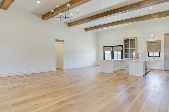 unfurnished living room with baseboards, light wood-style flooring, an inviting chandelier, beam ceiling, and recessed lighting