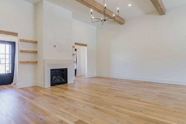 unfurnished living room with beam ceiling, light wood-style flooring, a high ceiling, a glass covered fireplace, and baseboards